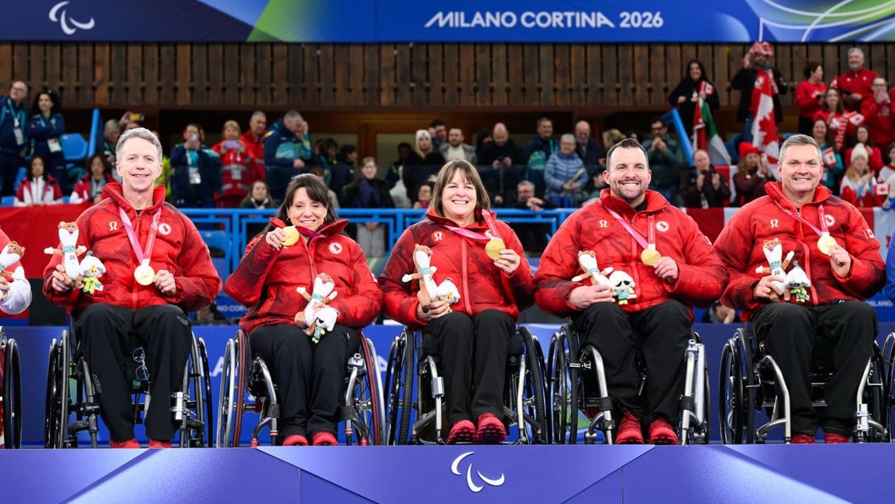 Five athletes in wheelchairs wearing red Team Canada jackets and black pants sit on a podium holding their medals