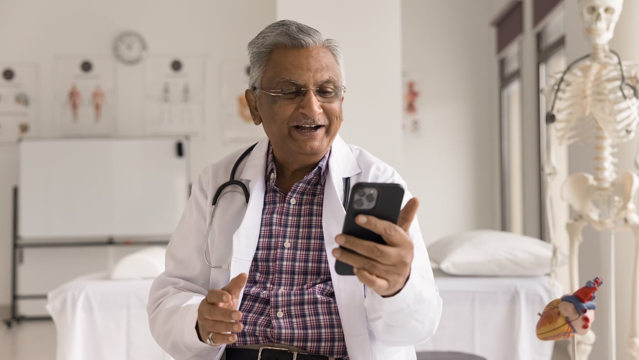 Older South Asian male doctor chatting happily on a video call with a patient