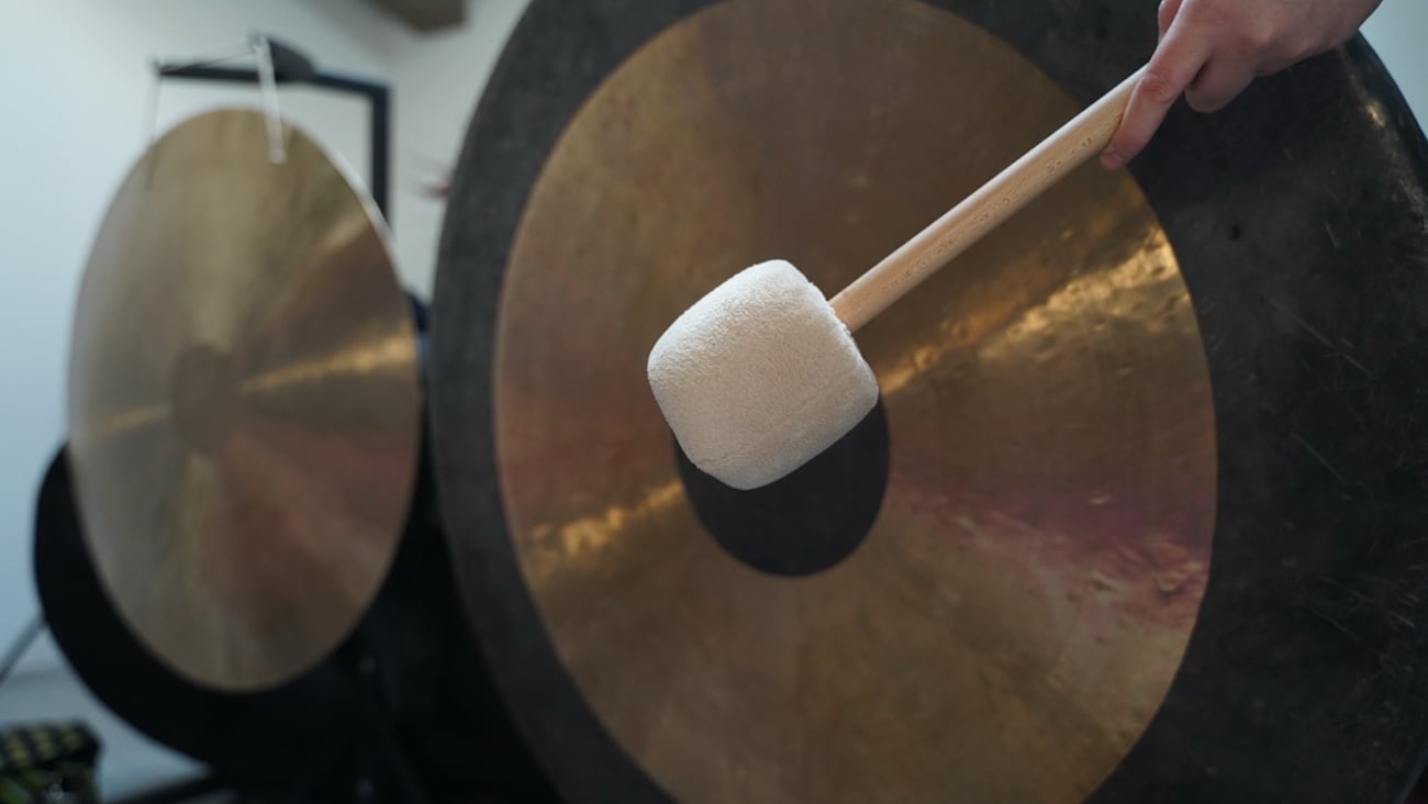 A person hits a gong with a mallet.