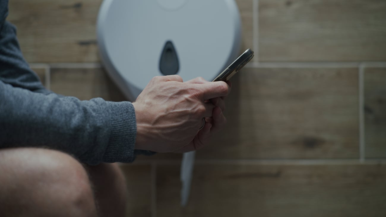 A man uses his phone while sitting on the toilet.