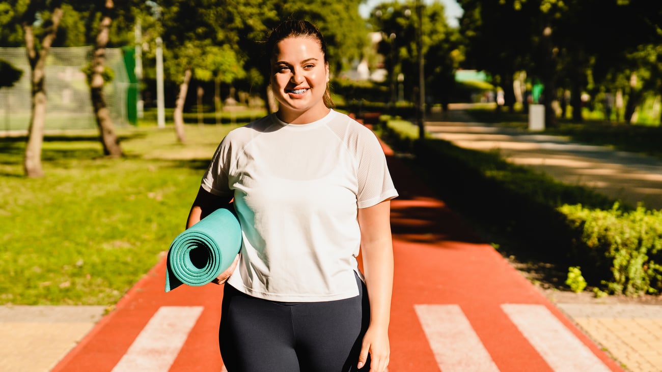 Young plus size woman carrying a yoga mat outside 