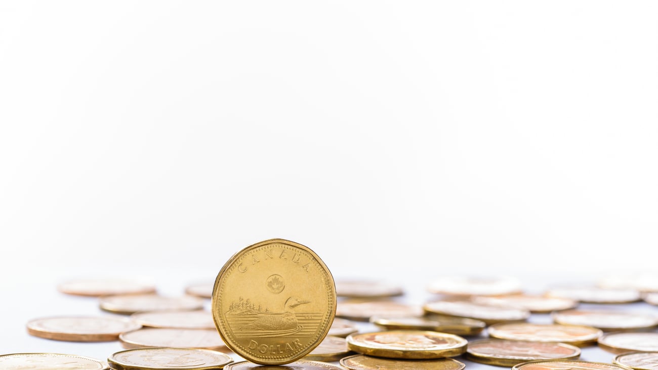 A loonie stands on its edge, next to a pile of other loonies