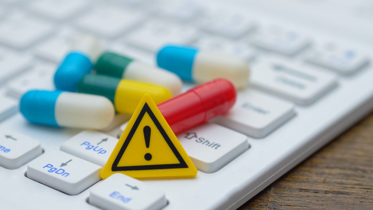 An exclamation mark sign and a pile of pills on a computer keyboard, representing the potential hazards of online drug information.