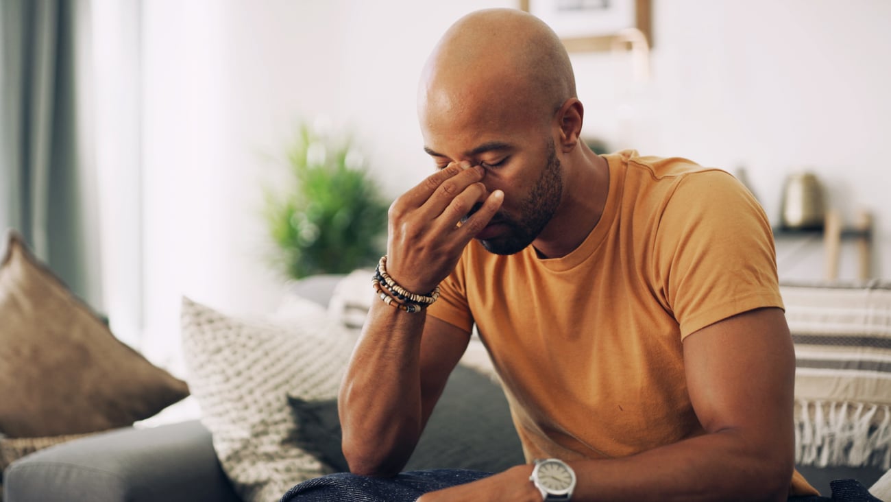 Young Black man in orange t-shirt holding his forehead because of sinus pain