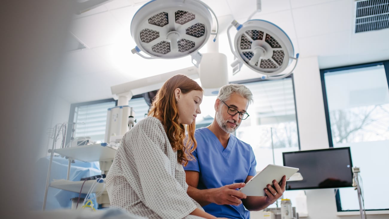 A young woman in a hospital gown in a procedure room discussing a chart with her doctor
