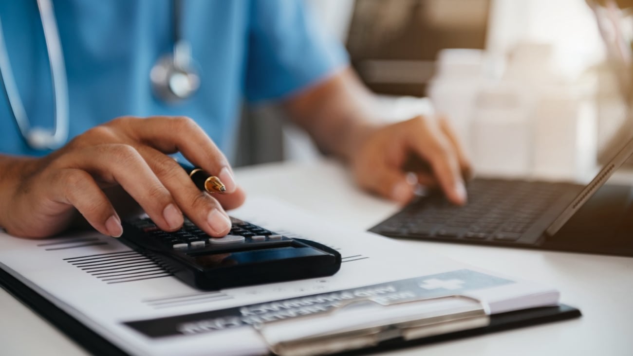 A doctor holding a calculator while on the computer.
