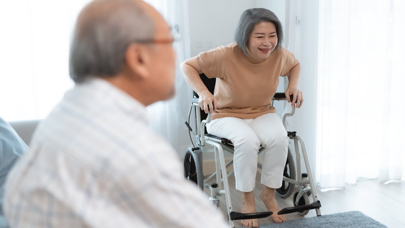 Older woman getting up out of a chair while her husband sits in the foreground
