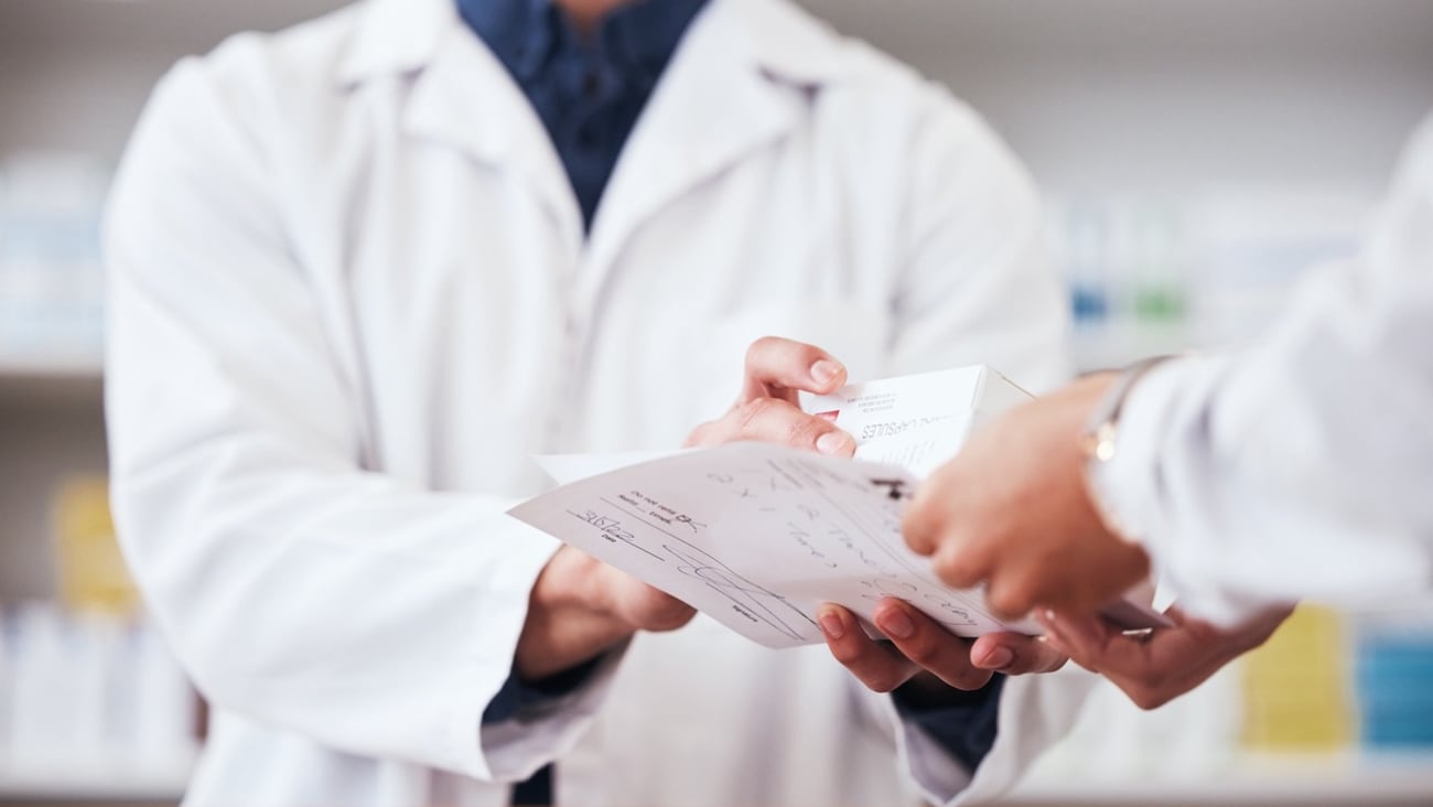 Closeup of pharmacist exchanging medication and a prescription.