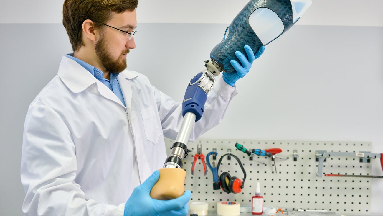 Portrait of young  prosthetics technician holding prosthetic leg  checking it for quality and making adjustments while working in modern laboratory, copy space