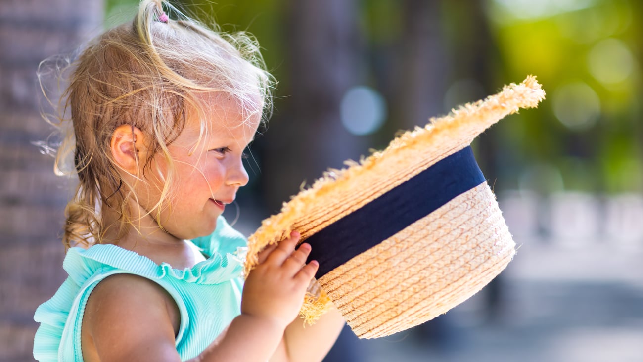 A little girl in a blue dress on a hot day holding a straw hat
