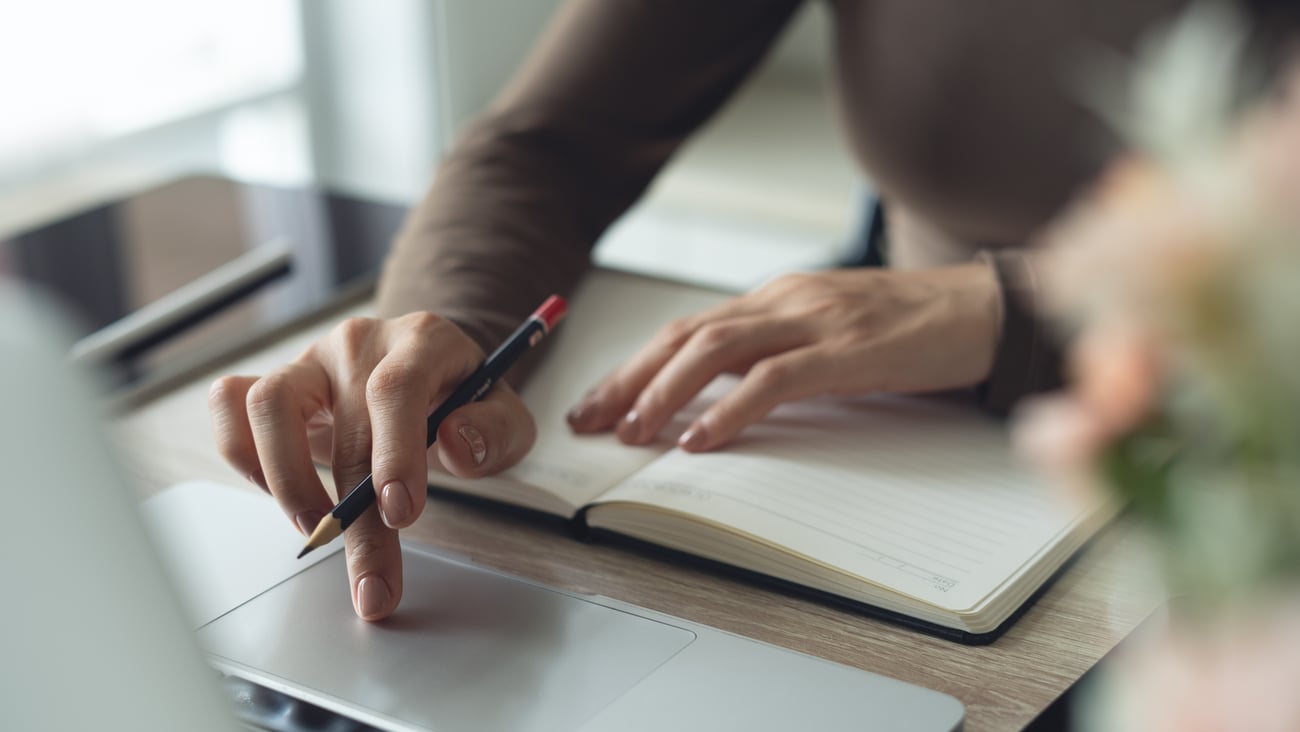 Young woman writing in a notebook and browsing a laptop