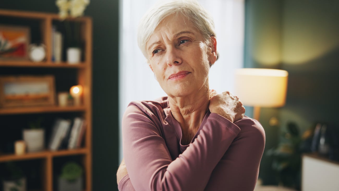 An older woman in a purple shirt holding her shoulder in discomfort