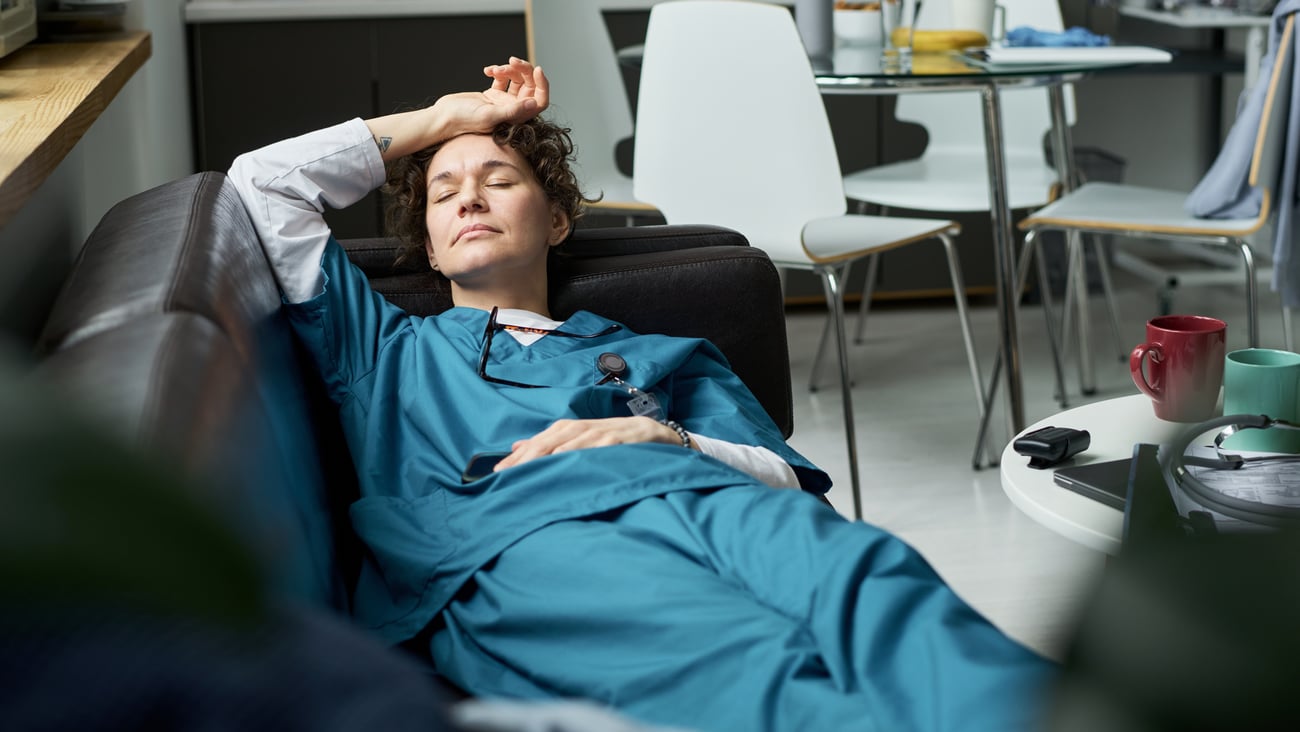 A woman doctor in blue scrubs taking a nap on a break room couch