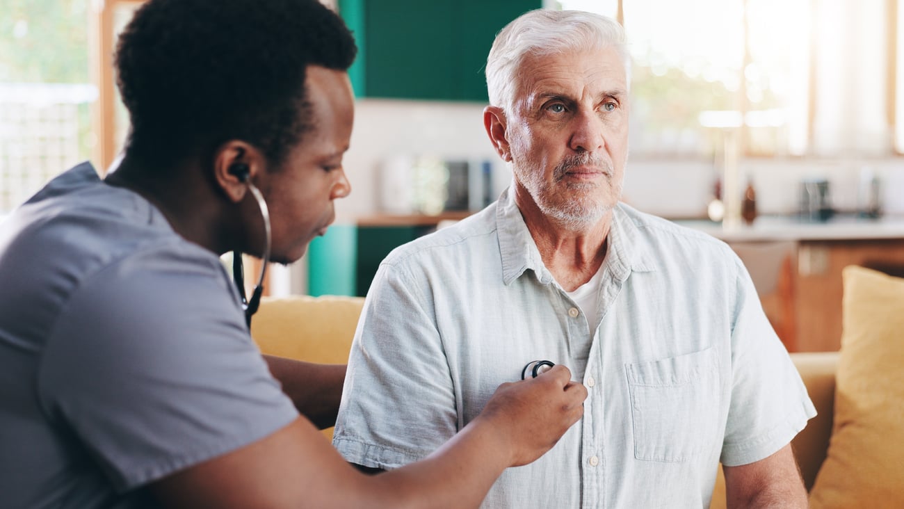 A young doctor listening to an older male patient's heart