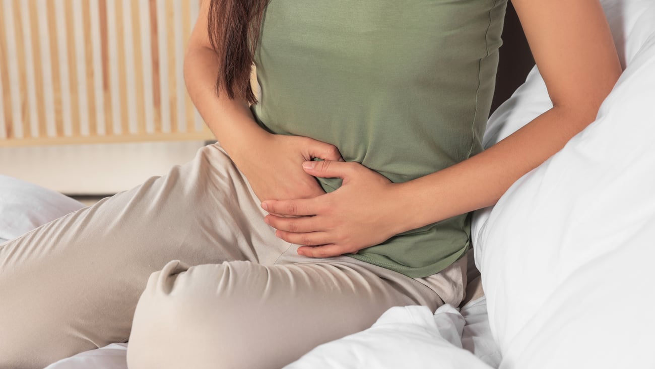 Young woman in a green shirt holding her stomach in discomfort
