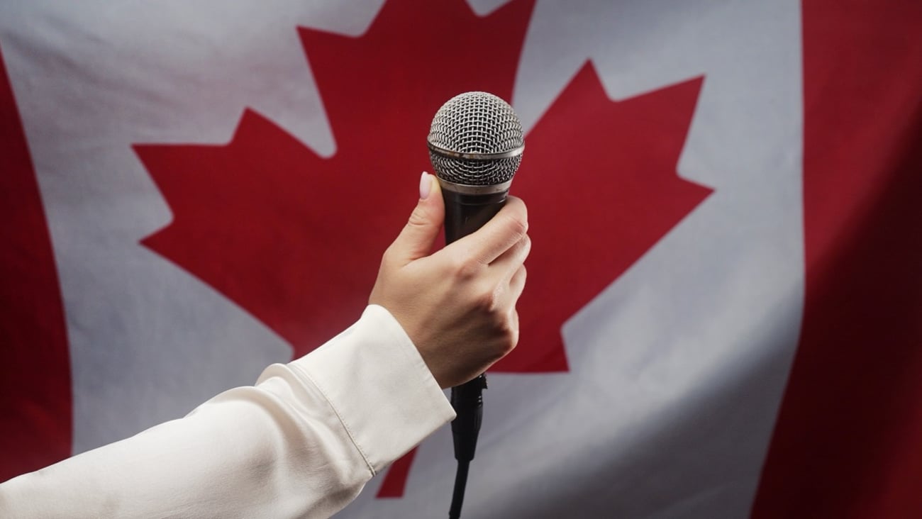 A hand holds a microphone in front of the Canadian flag