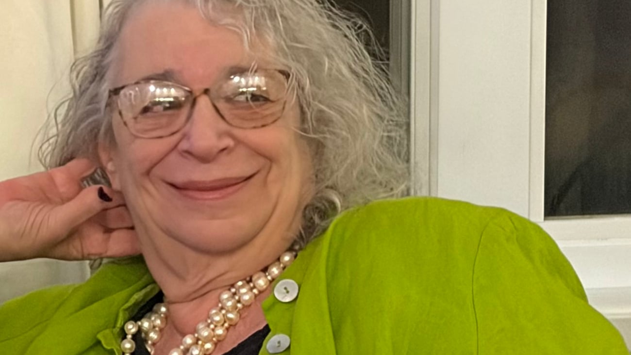 Dr. Perle Feldman in a green shirt and pearls, reclining on a sofa