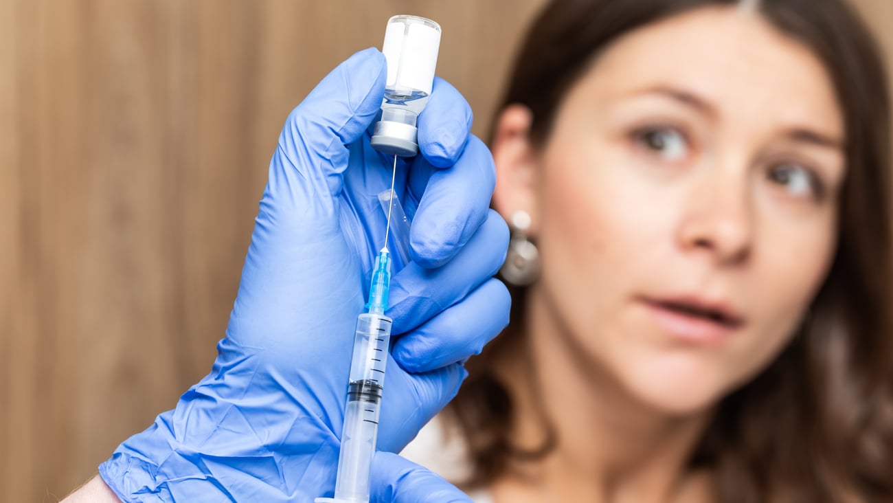 A woman looking worried as a pharmacist fills a syringe