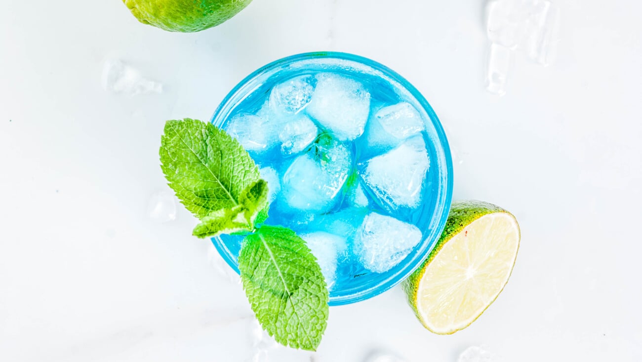 Colorful summer beverage, iced blue lagoon alcohol cocktail drink with lime and mint, white marble background copy space; Shutterstock ID 1196929978