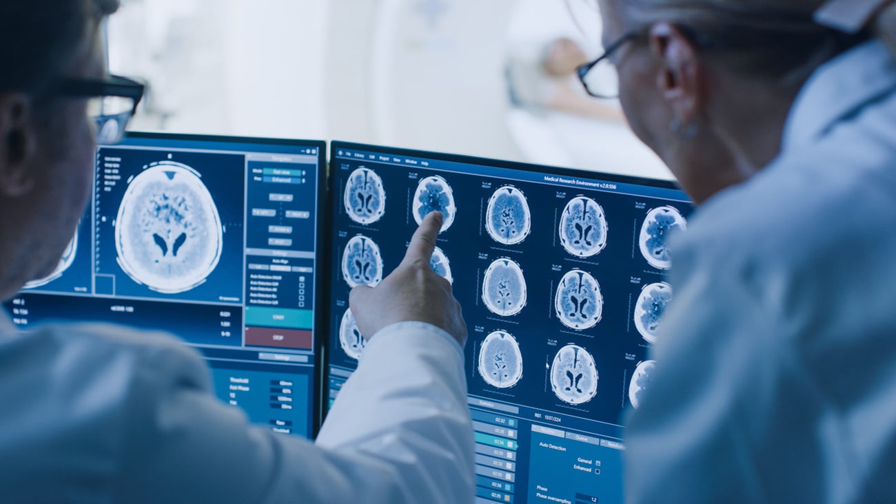 In Control Room Doctor and Radiologist Discuss Diagnosis while Watching Procedure and Monitors Showing Brain Scans Results, In the Background Patient Undergoes MRI or CT Scan Procedure.; Shutterstock ID 1243951690