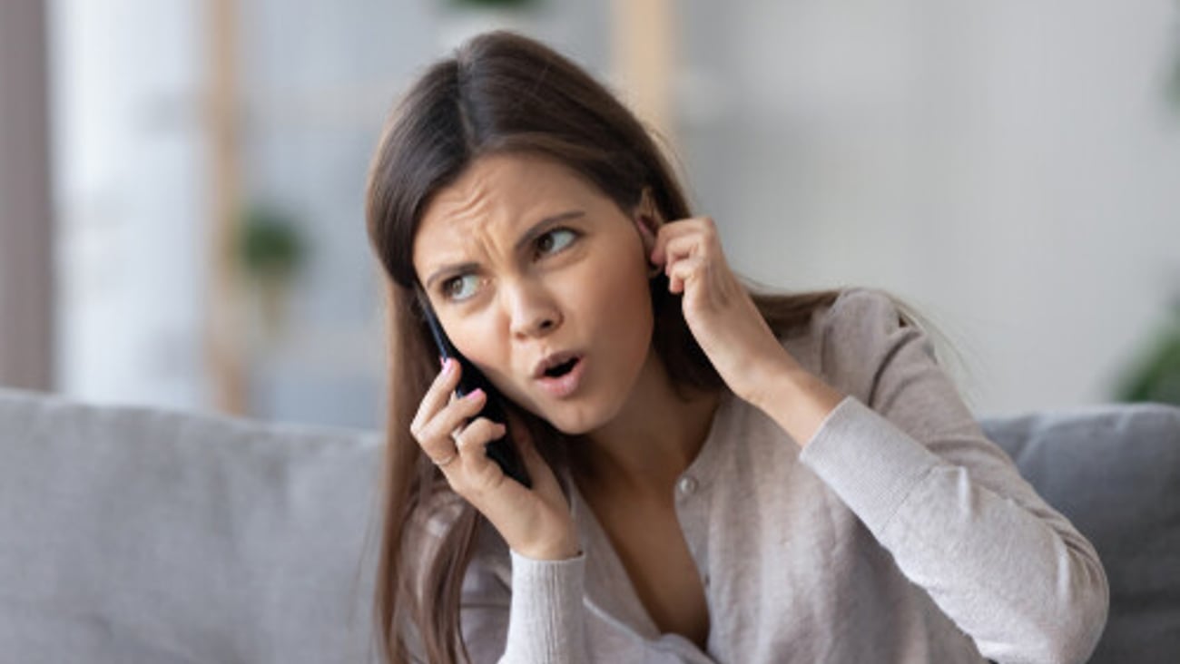 Annoyed young woman talking on the phone not hearing bad signal lost no mobile connection on cellphone, irritated girl closing ear frustrated by communication telecommunication service problem indoor; Shutterstock ID 1297544935