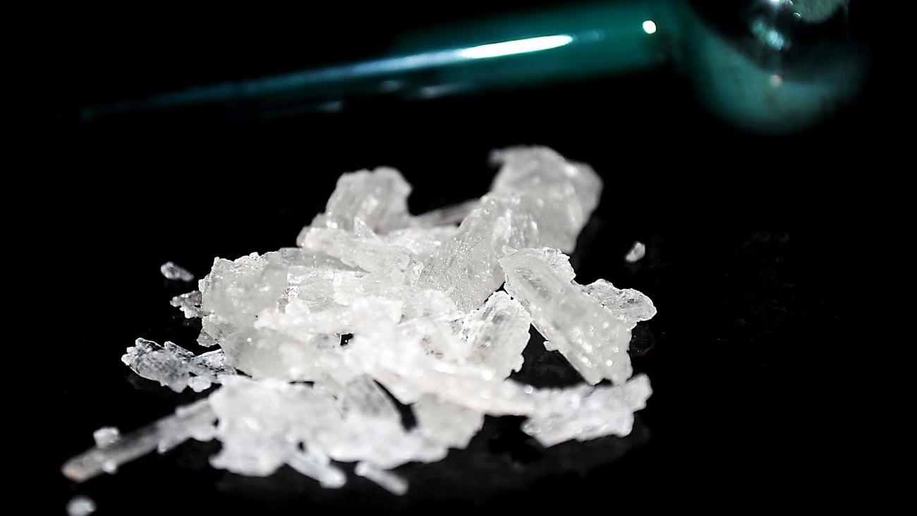 Small pile of methamphetamine crystals with blue glass meth pipe in background.; Shutterstock ID 1314852365