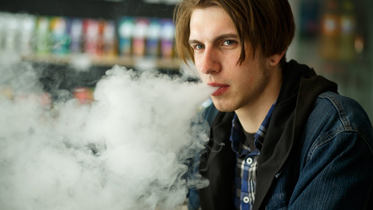 Vape teenager. Portrait of young handsome guy smoking an electronic cigarette in the vape bar. Bad habit that is harmful to health. Vaping activity. Close up.; Shutterstock ID 1400133746
