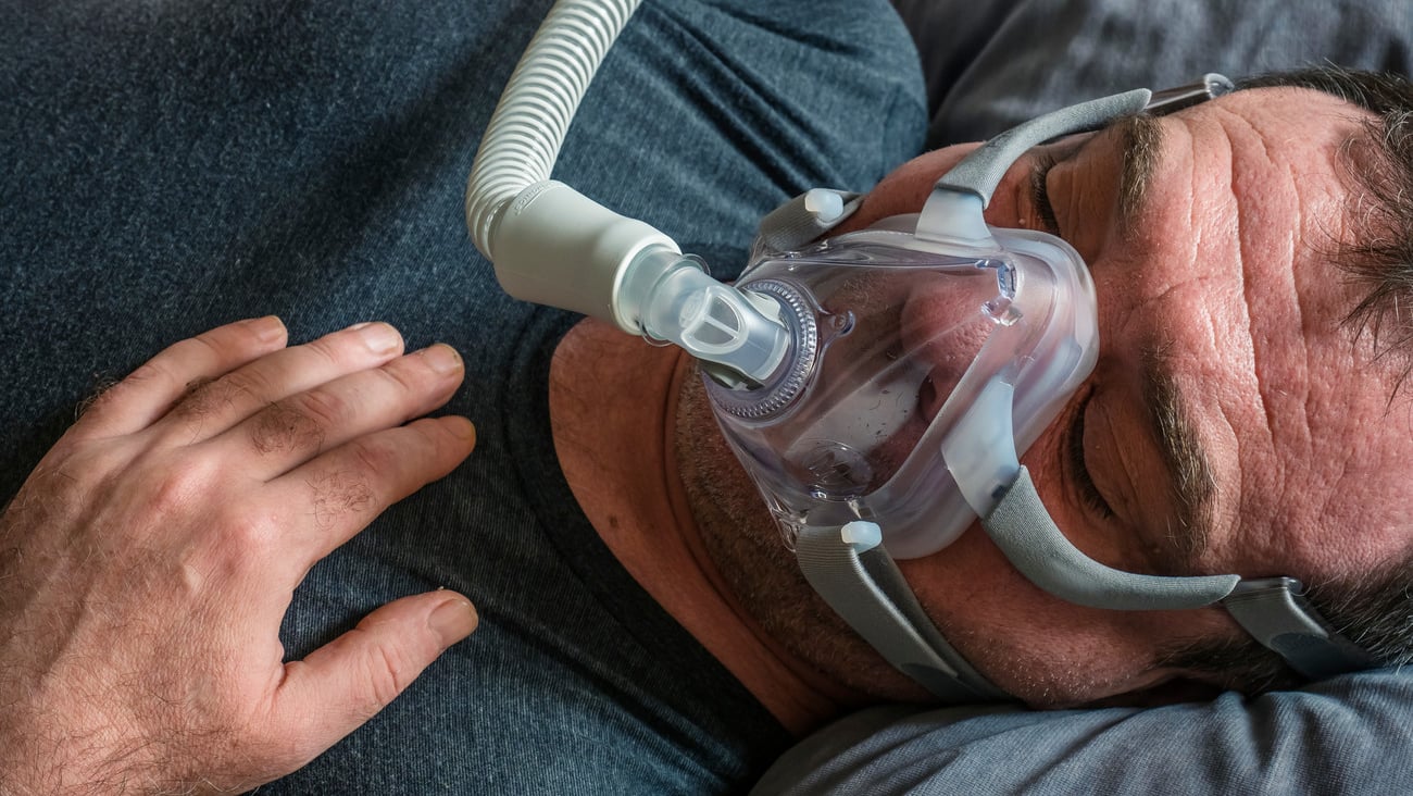 A man in an oxygen mask for CPAP therapy in bed; Shutterstock ID 1675350667