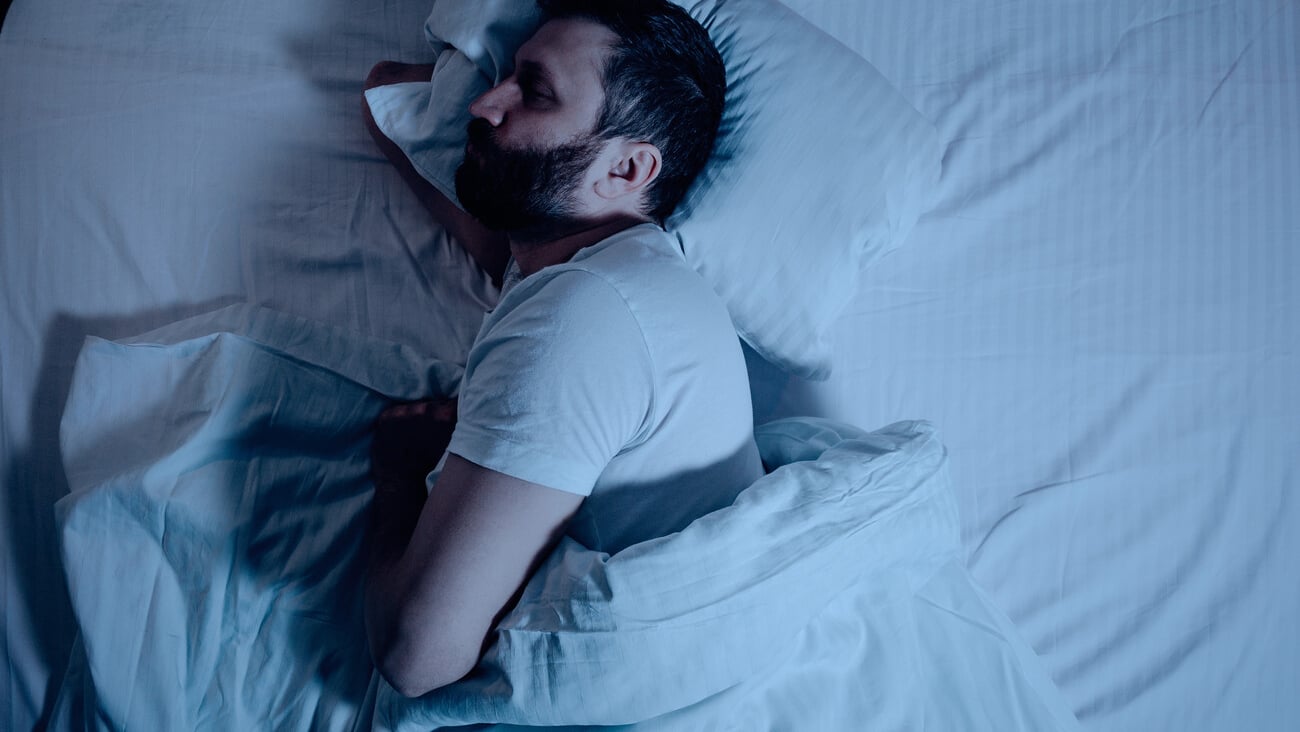 A lonely bearded dark-haired man sleeps soundly on his stomach at night on the bed. General plan from above, orthopedic pillow, bedroom, self-isolation. One; Shutterstock ID 1691821795