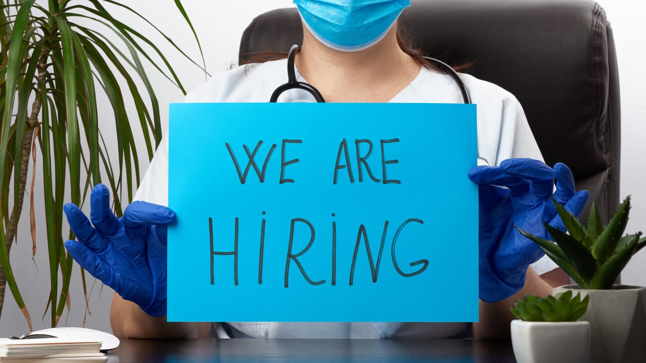 woman doctor in a white coat, sterile medical gloves holds a poster with the inscription we are hiring, concept of staffing, lack of personnel in medicine; Shutterstock ID 1735283411