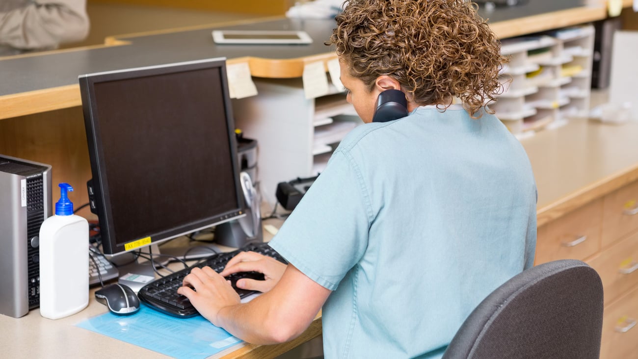 Rear view of female nurse answering telephone while working on computer at hospital reception; Shutterstock ID 177739580