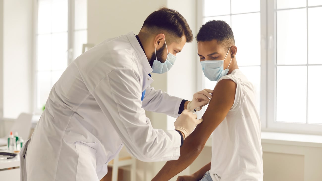 Doctor in medical face mask giving injection to patient during vaccination campaign at the clinic. Young African-American man getting Covid-19, AIDS or flu antivirus vaccine shot at the hospital; Shutterstock ID 1874064979