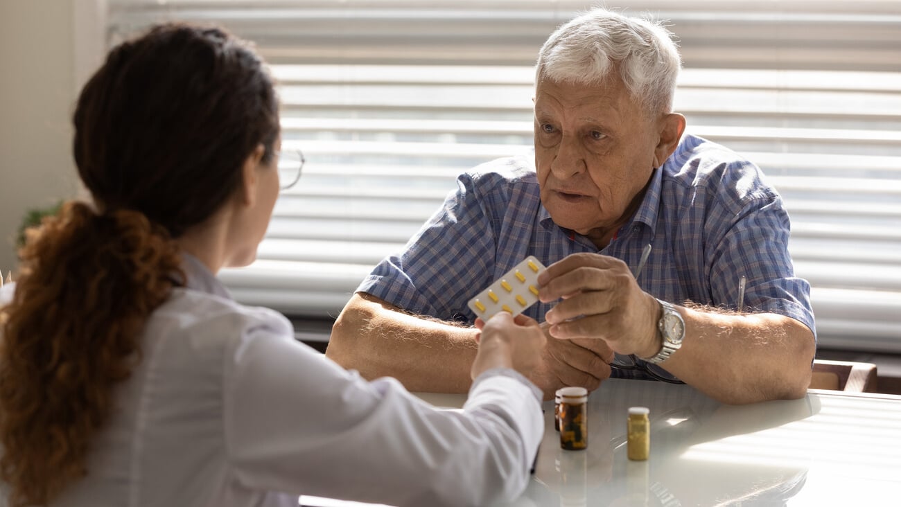 Woman GP or therapist give recommend pills or drugs to unhealthy mature male patient in clinic. Caring female doctor prescribe medicines to sick senior man client. Elderly healthcare concept.; Shutterstock ID 1879850251