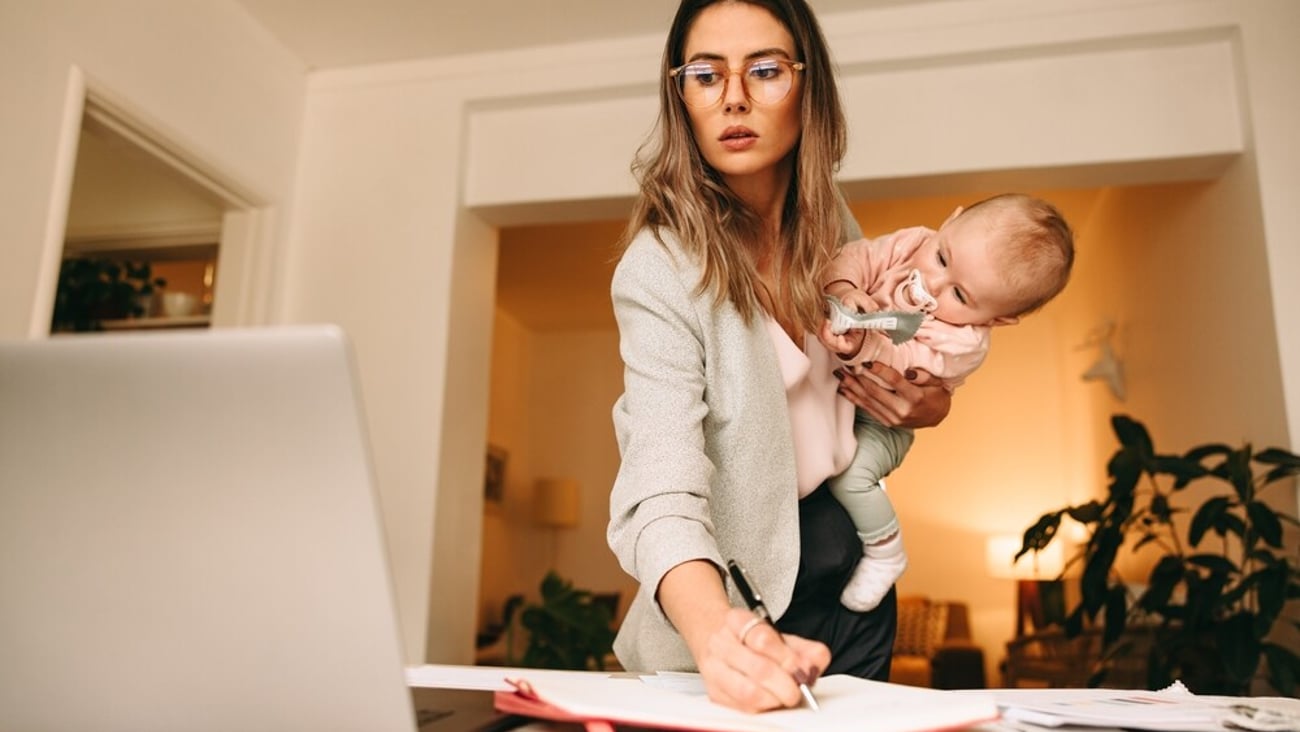Design professional making notes while holding her baby. Multitasking mom planning a new project in her home office. Creative businesswoman balancing work and motherhood.; Shutterstock ID 2084661583