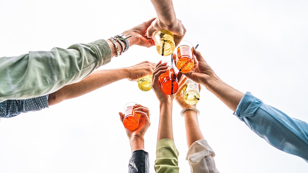 Best friends raising cocktail glasses celebrating a toast - closeup on the hands - arms up against a white sky background - people using alcohol and alcoholic drinks concept; Shutterstock ID 2161015131