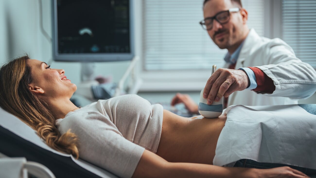 Pregnant woman undergoing ultrasound test at gynecologist office. Closeup of male doctor moving ultrasound probe on pregnant woman's stomach in hospital. Doctor and patient. Ultrasound equipment. ; Shutterstock ID 2265937089