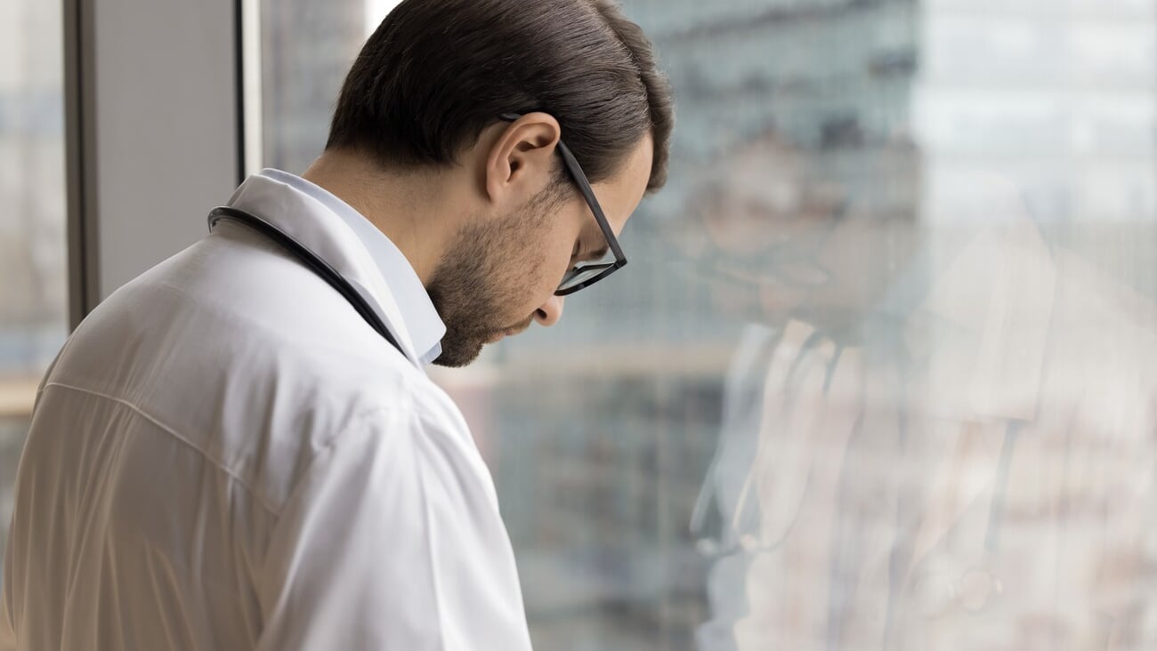Tired frustrated young doctor man standing at window with closed eyes and head bended down, thinking on problems, practitioner mistake, failure, loss of patient, feeling despair, stress; Shutterstock ID 2415509351