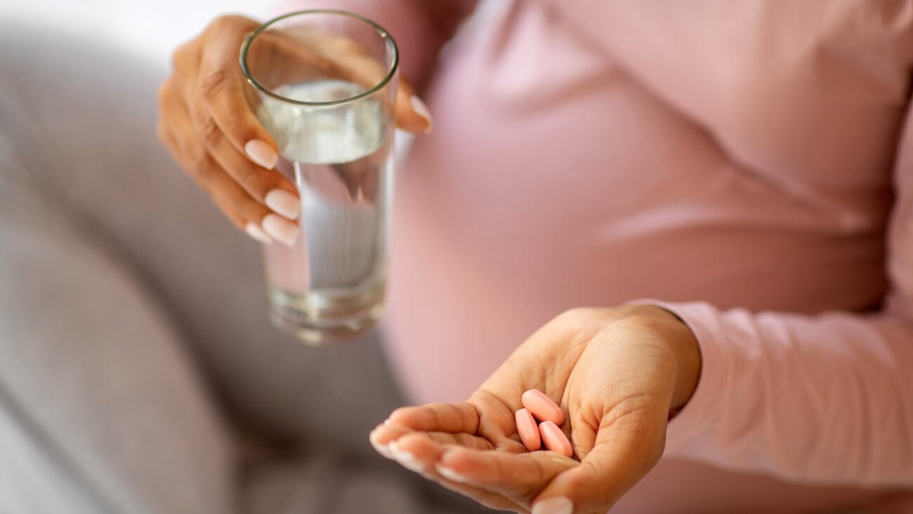 Prenatal Vitamins And Supplements. Unrecognizable black pregnant woman taking pills and glass of water, cropped shot of young expectant mother using medicaments for healthy pregnancy, closeup; Shutterstock ID 2424227009