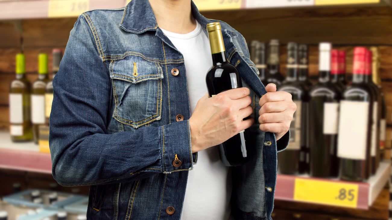 man in a supermarket stealing a bottle of champagne; Shutterstock ID 246155941
