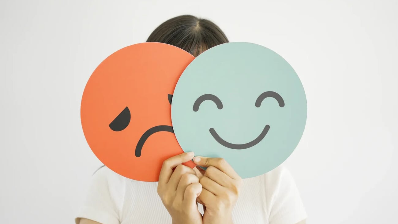 Woman hands holding sad face hiding behind happy face, bipolar and depression, mental health, split personality, mood change concept