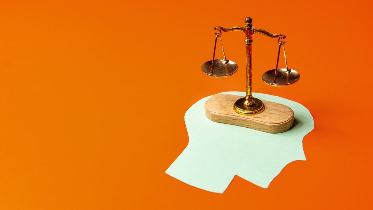 Balance scale placed on top of a green paper cutout shaped like a human head. Weighing options, rational thinking, decision-making concept.; Shutterstock ID 2529244839