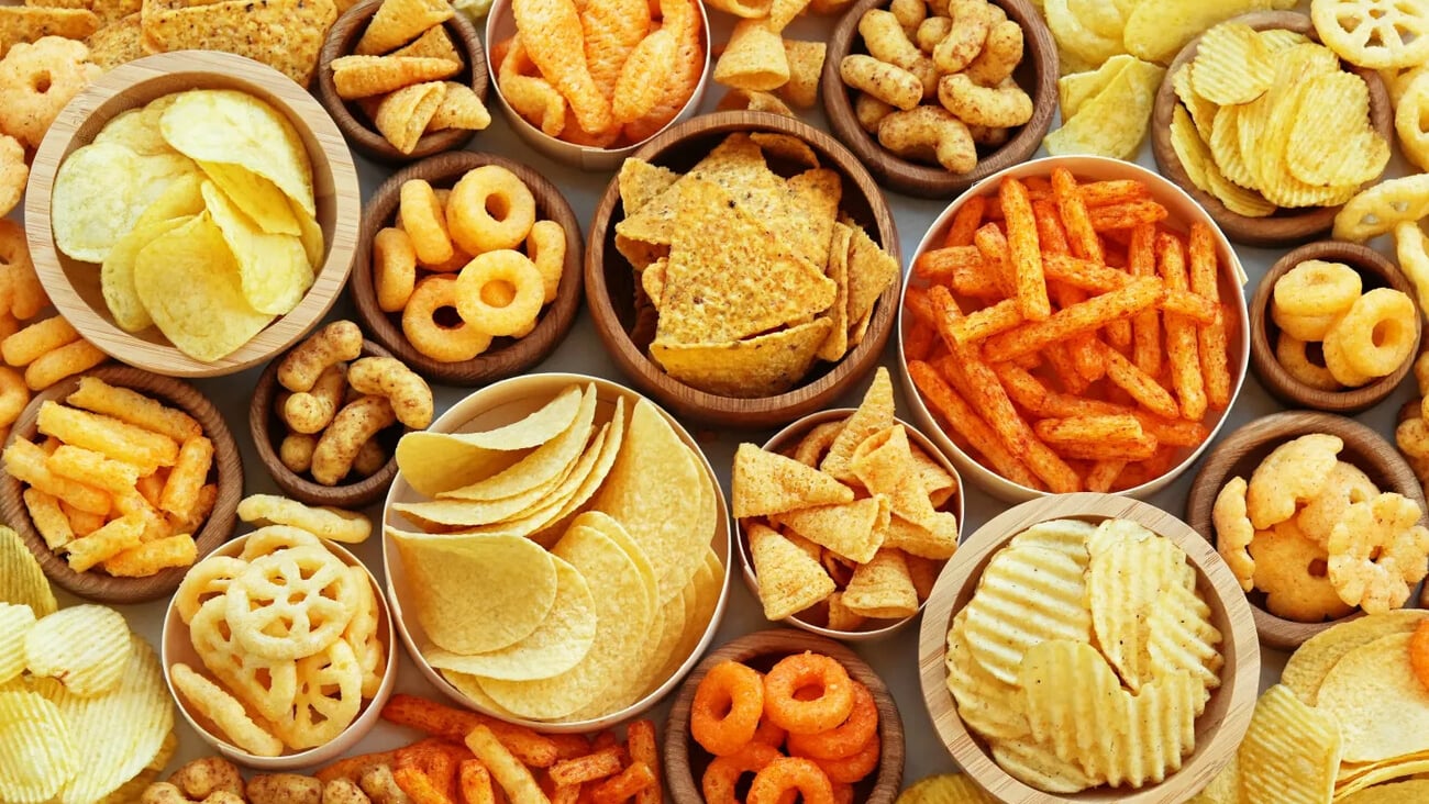 Colorful mix of salty snacks for beer varieties: chips and pretzels, onion rings and crackers. Non-healthy junk food background; Shutterstock ID 2593468019