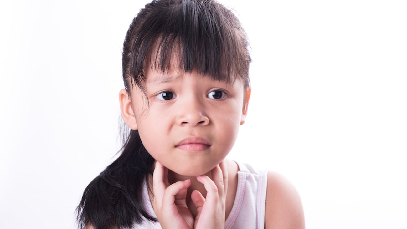 A school-aged girl holds her throat.