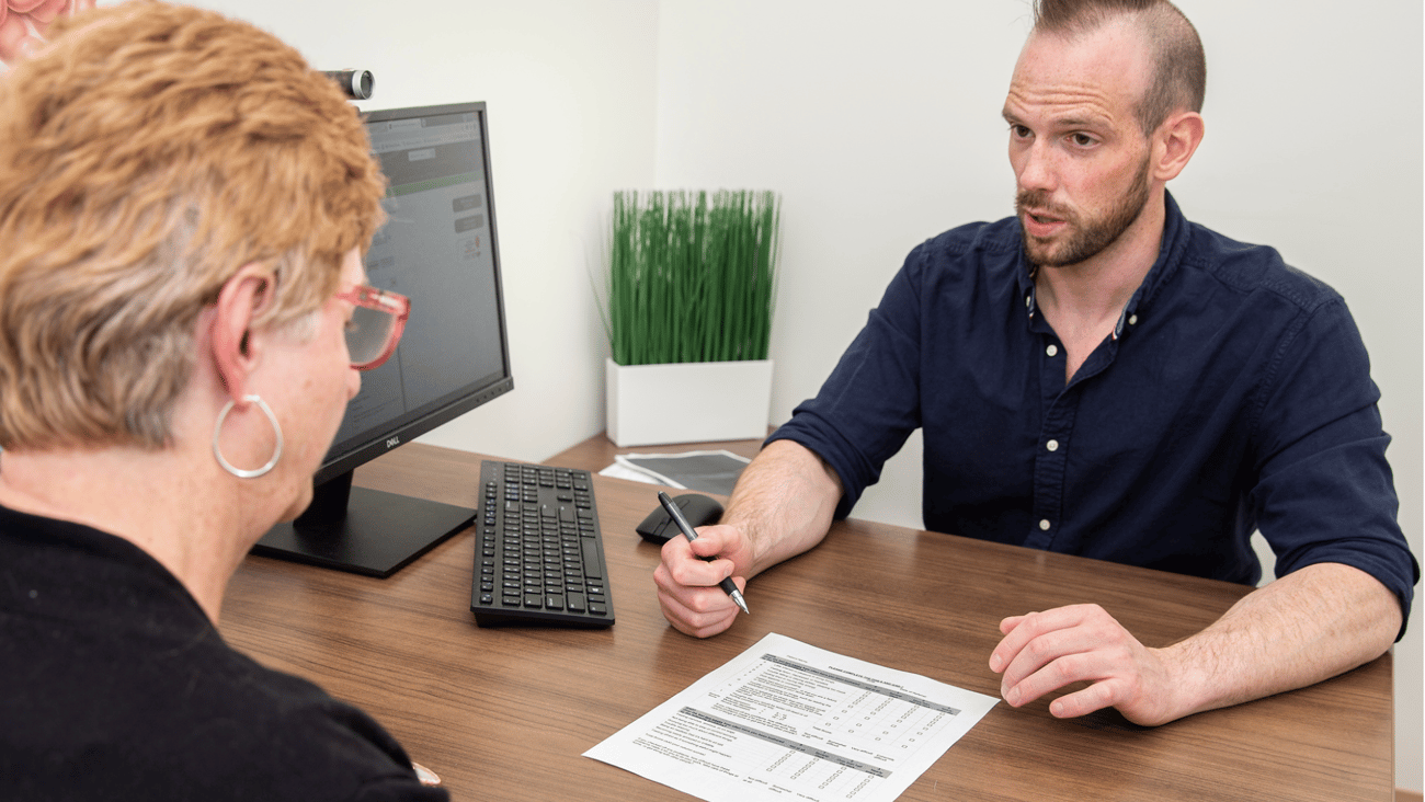 A woman at a desk with a pharmacist in black shirt, a paper in front of them