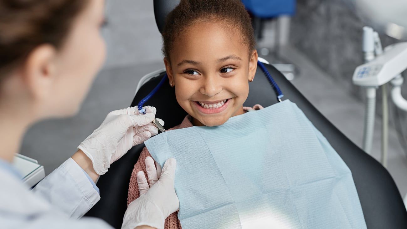 smiling child in dentist chair with dentist looking at her