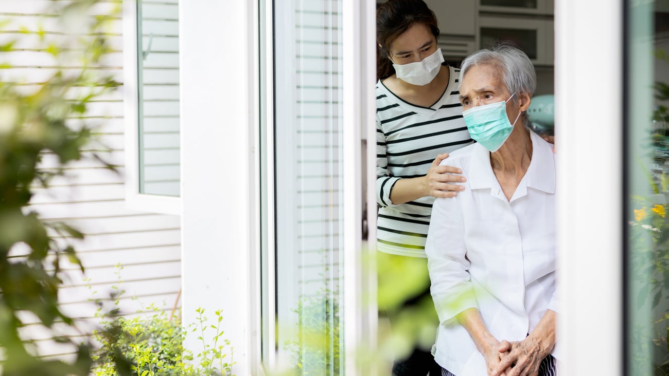 An elderly woman and younger woman a window wearing. masks