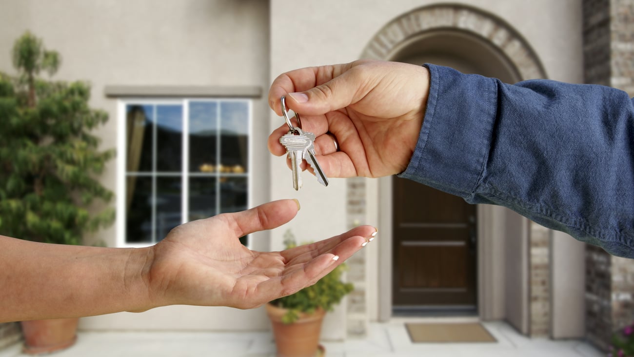 One hand giving another hand keys, with house in background