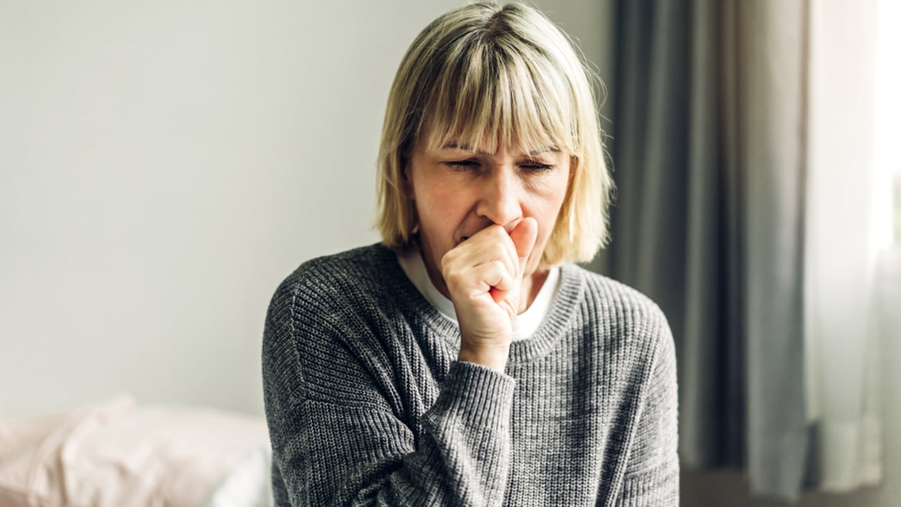 A woman in gray sweater coughing into her hand