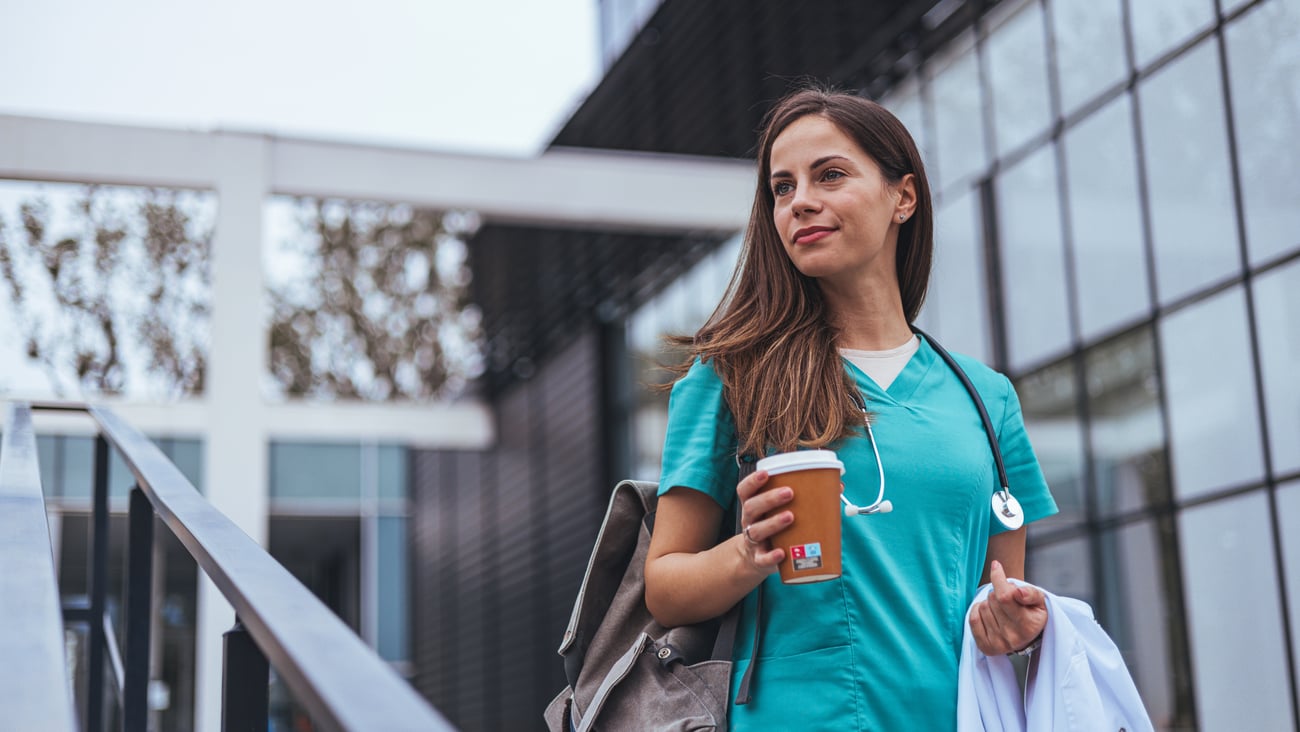 Young female doctor in scrubs carrying coffee outside going or coming from work