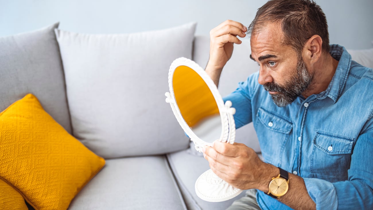 Middle aged man worried about male pattern baldness looking in a mirror